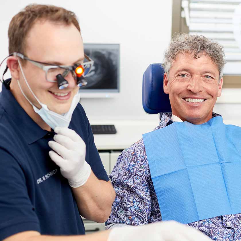 Mitarbeiterin und Dr. Schmidt mit Lupenbrille während der Behandlung eines Patienten