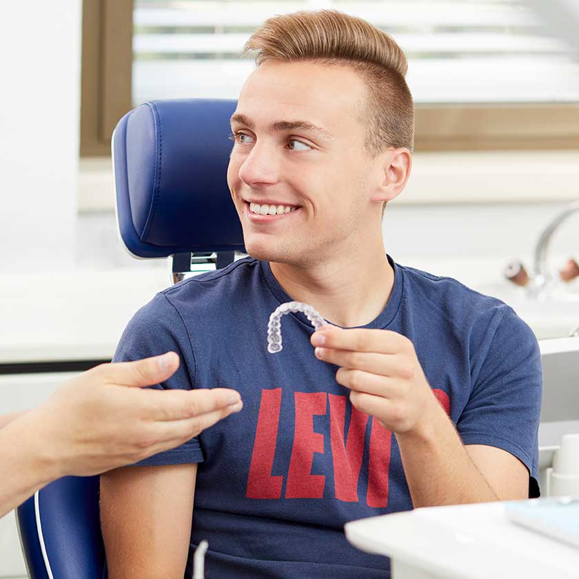 Lächelnder Patient auf Behandlungsstuhl mit Harmonischiene® in der Hand. 