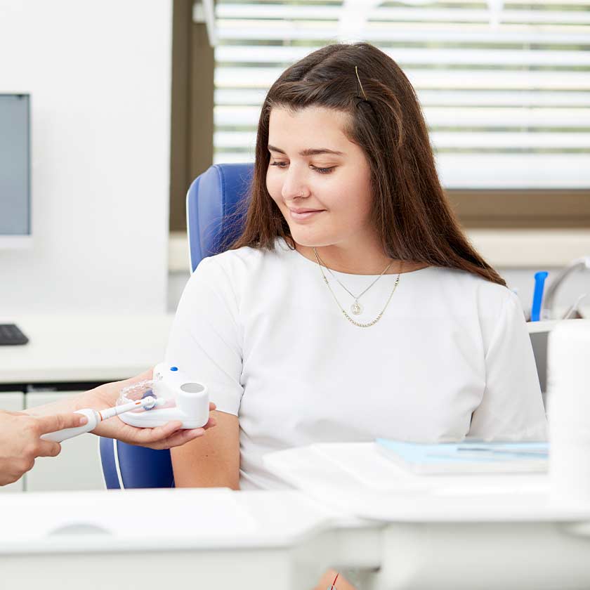 ZfA erläutert Patientin mit Zahnbürste und Gebissmodell die richtige Putztechnik zur Vorbeugung von Parodontitis