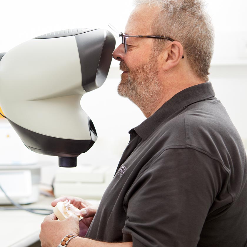 Zahntechniker im Dentallabor begutachtet durch Gerät Zahnabdruck