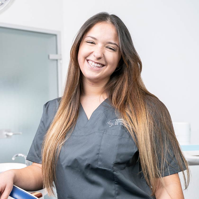 Lächelnde ZfA lehnt an einen Behandlungsstuhl in der Wormser Zahnarztpraxis am Lutherdenkmal